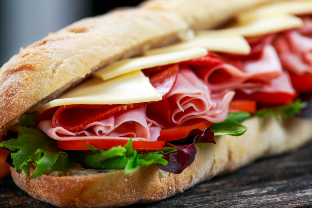 Sandwich with lettuce, slices of fresh tomatoes, salami, hum and cheese.
